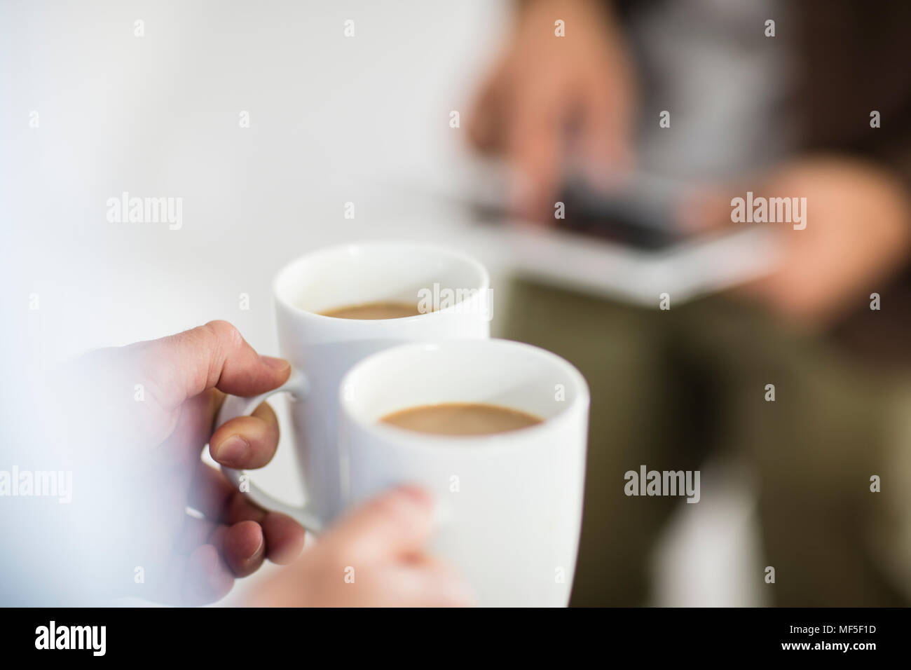 Close-up of woman holding coffee cups while man using tablet in office Stock Photo