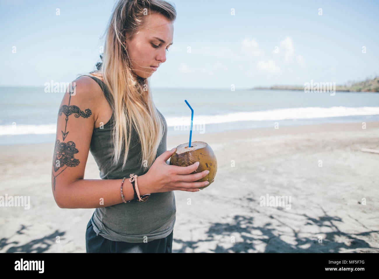 Cuba, Young woman with tattoo at Playa de Miel drinking coconut water Stock Photo