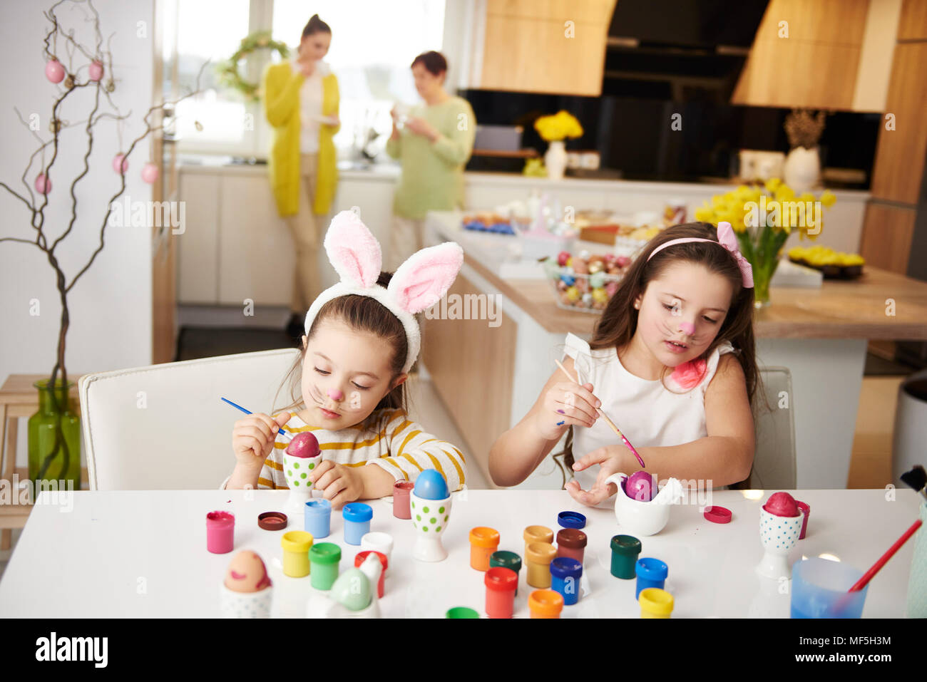 Sisters sitting at table painting Easter eggs Stock Photo