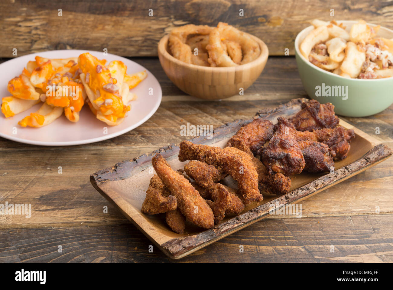 Typical american food, potatoes with cheese and bacon, fried onion rings and chicken wings Stock Photo