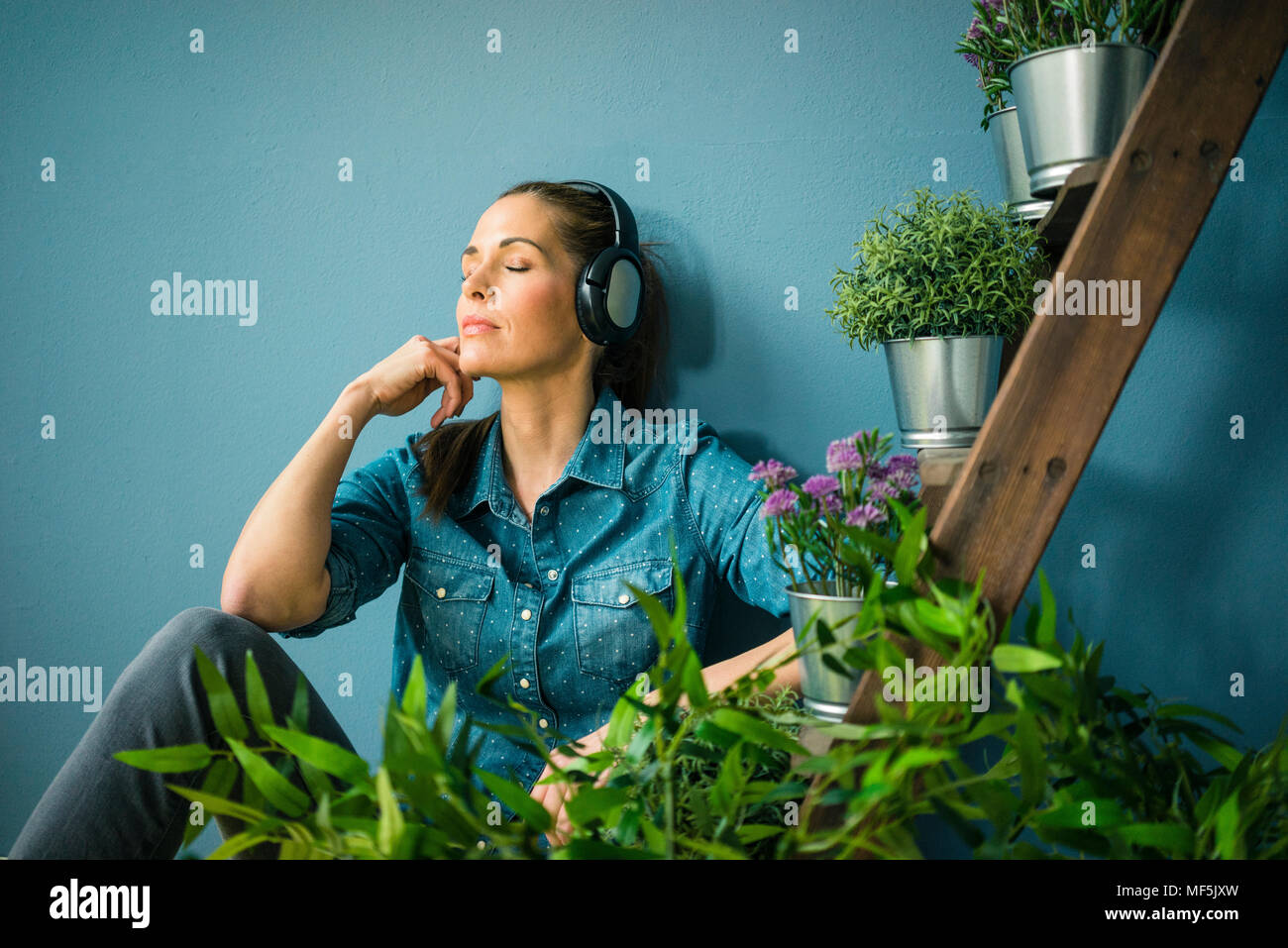 Beautiful woman in her home, decorated with plants, listening music with headphones Stock Photo