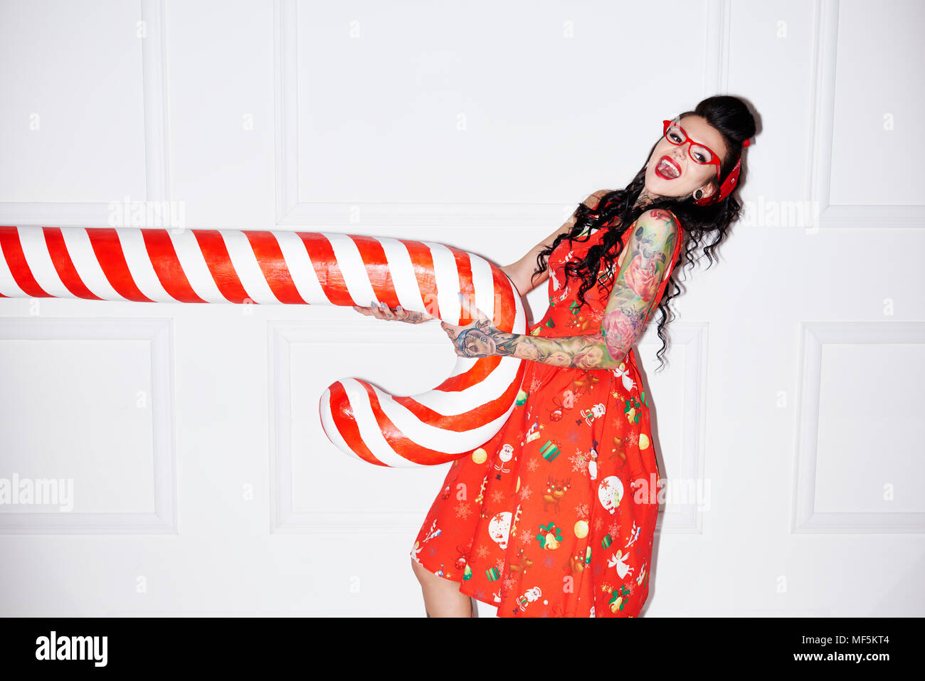 Portrait of tattooed woman having fun with oversized candy cane Stock Photo