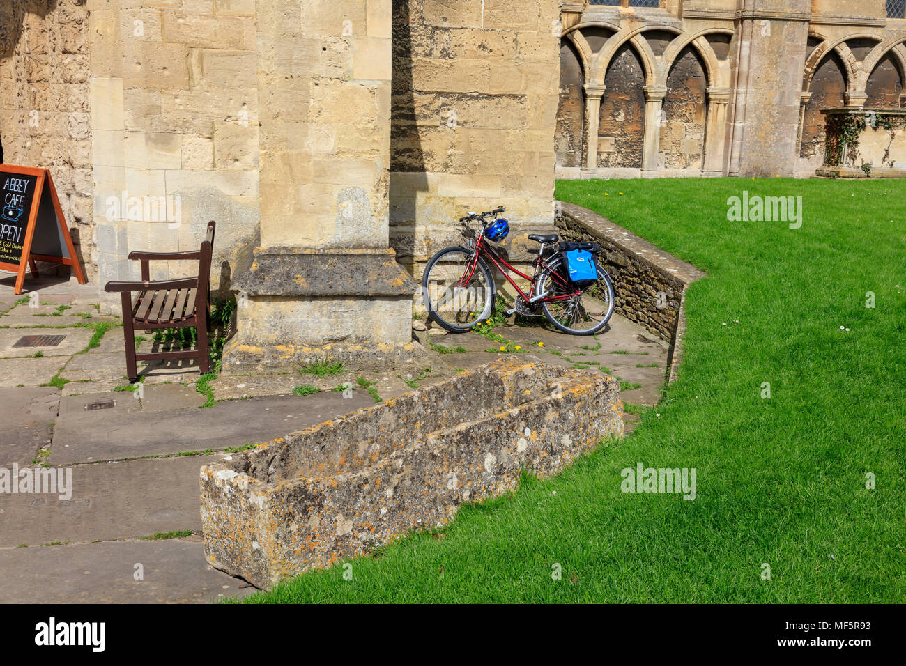 A cyclist leaves a bike propped up against the wall of Malmesbury Abbey while they visit, Wiltshire, UK Stock Photo