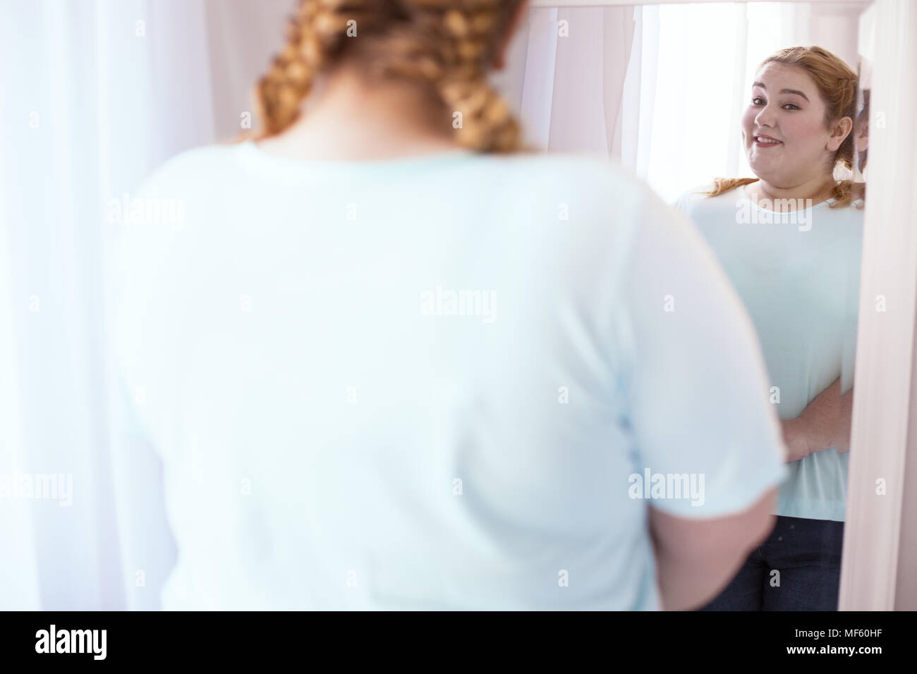 Smiling young woman watching herself in the mirror Stock Photo