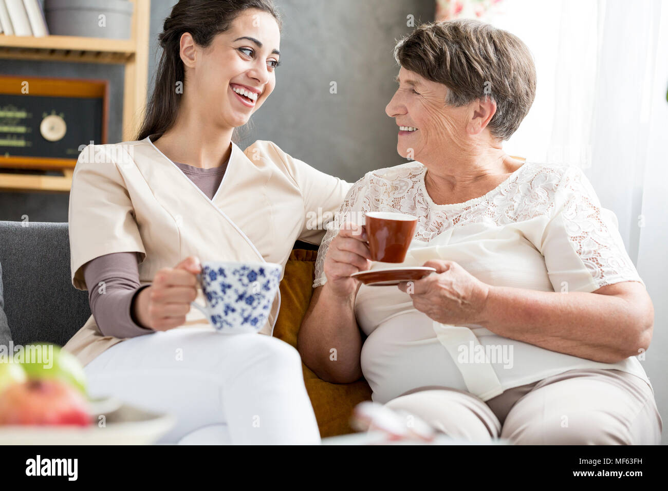 Smiling volunteer drinking coffee with a senior patient in a nursing home Stock Photo