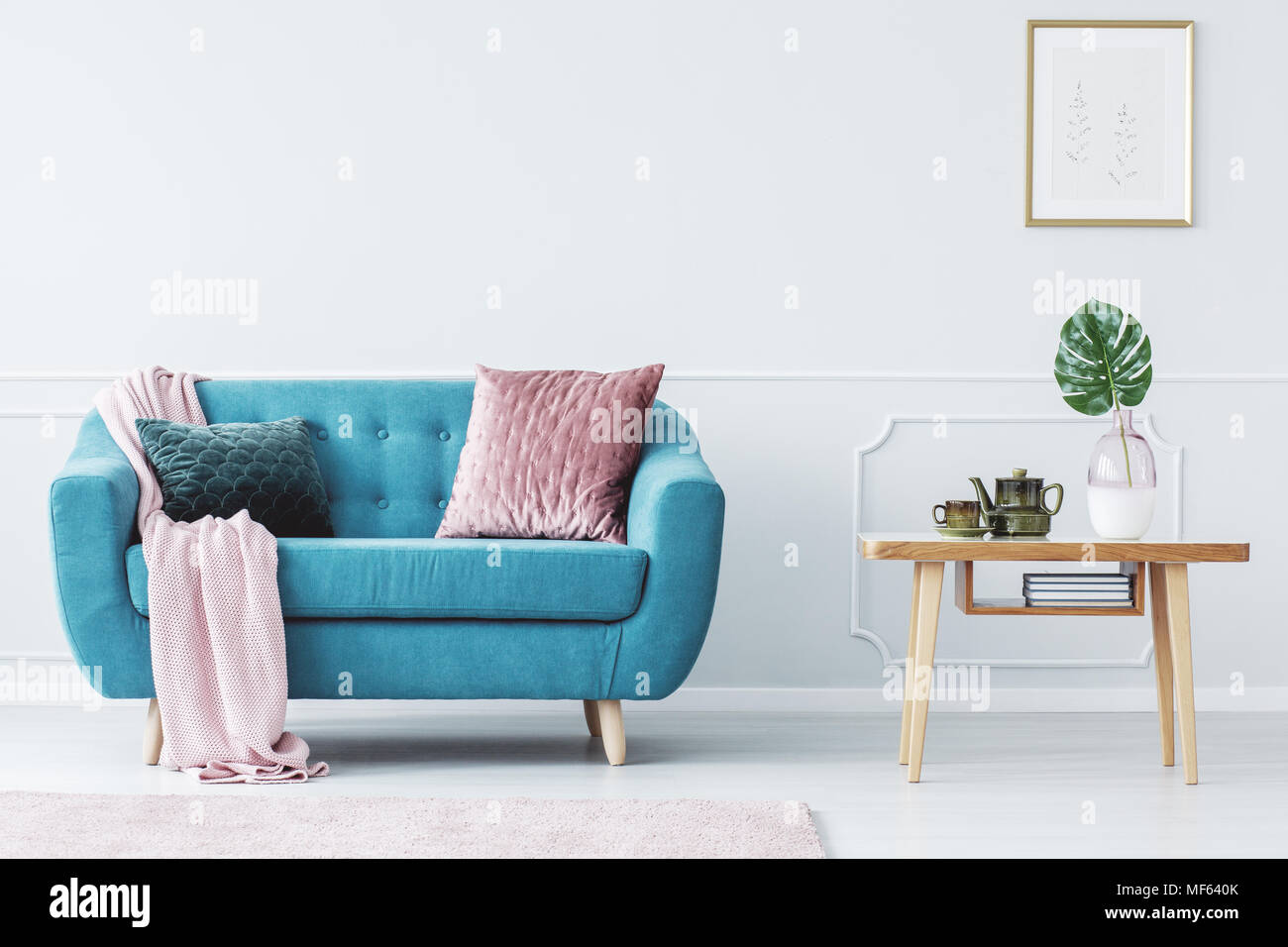 Pink pillow on turquoise couch next to wooden table in pastel