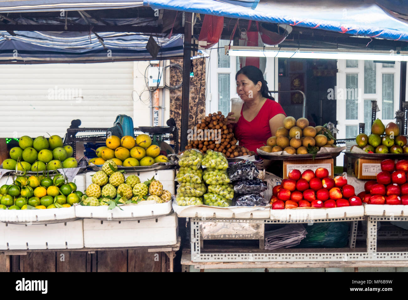 A female stall holder drinking a beverage in her fruit and vegetable stall in the Ton That Dam Street markets, Ho Chi Minh City, Vietnam. Stock Photo