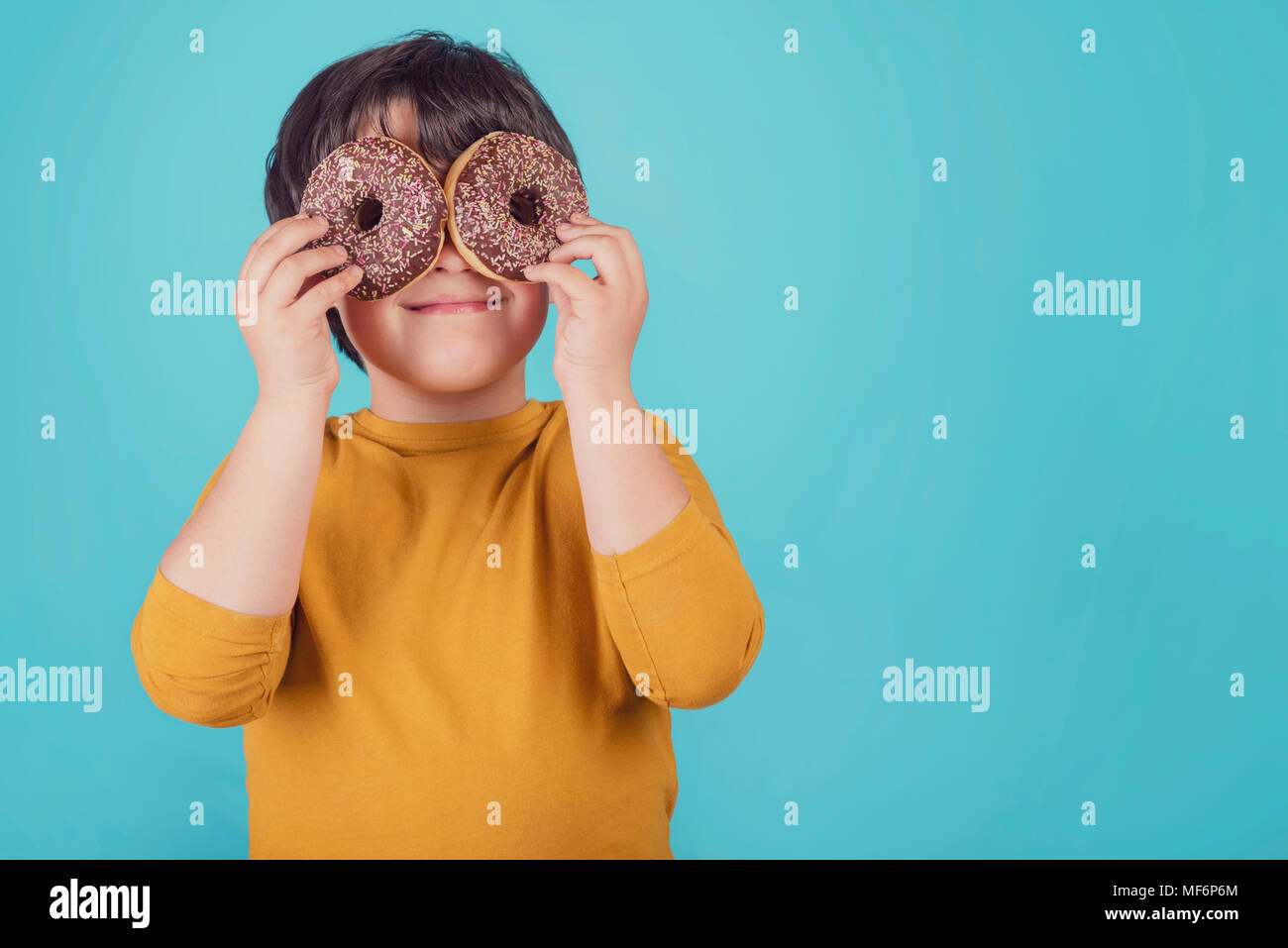 smiling boy holding donuts over her eyes Stock Photo
