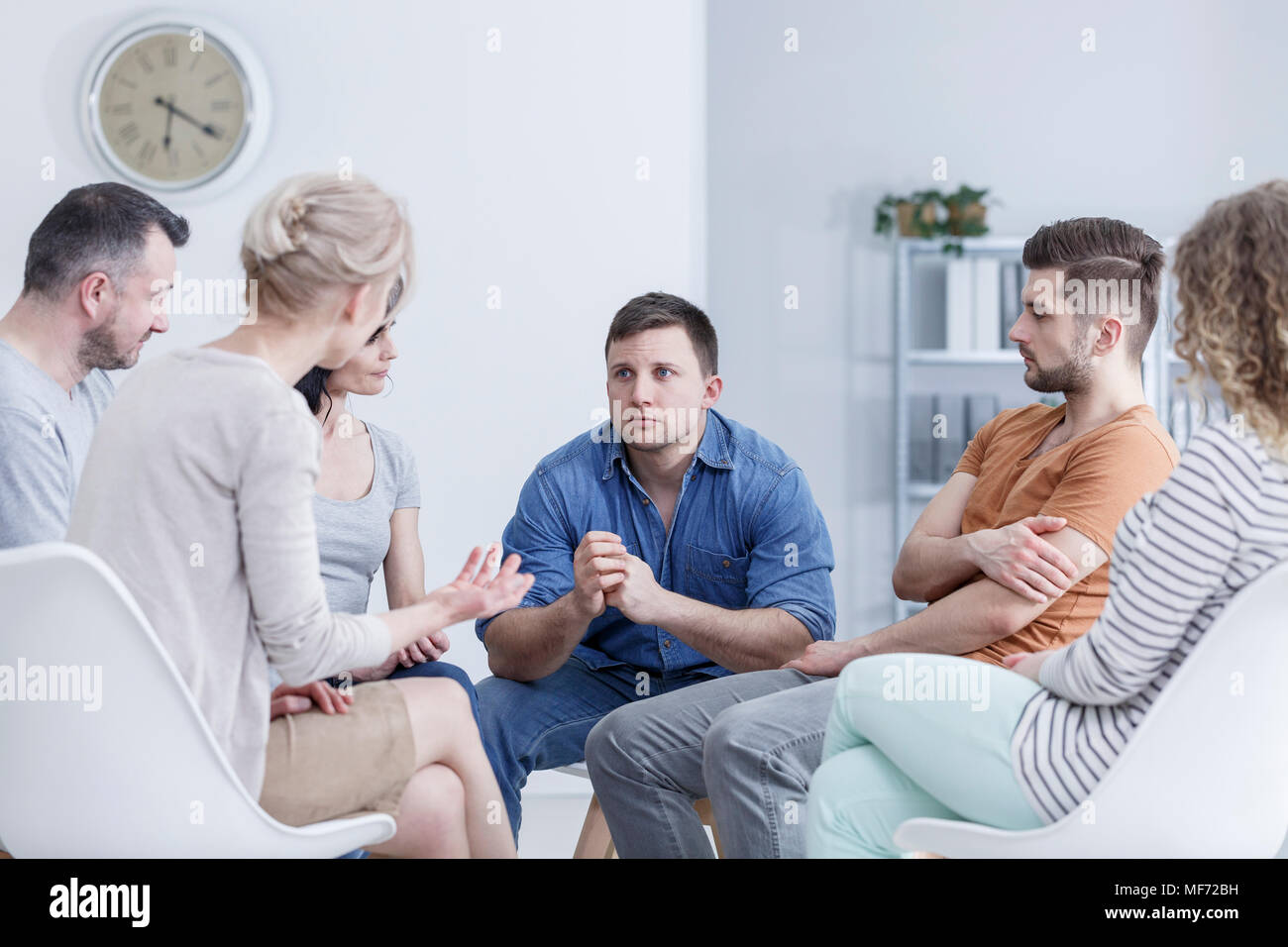 Sad, young man sitting in a bright office during a group meeting for gambling addicts Stock Photo