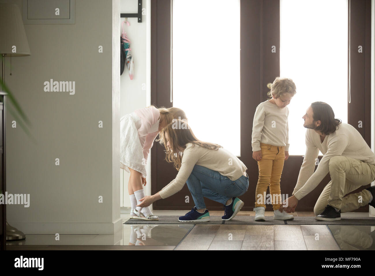 Parents helping son and daughter put shoes on at home Stock Photo