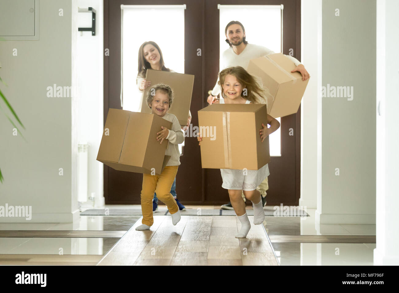Excited kids running holding boxes, family moving in new house Stock