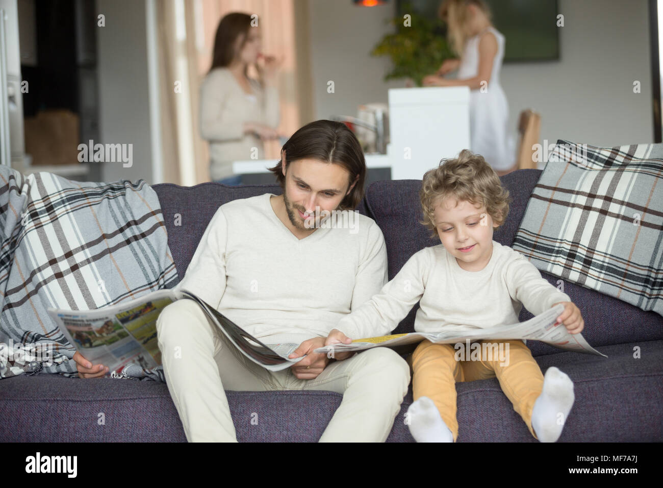 Little son pretending reading newspaper sitting on couch with fa Stock ...