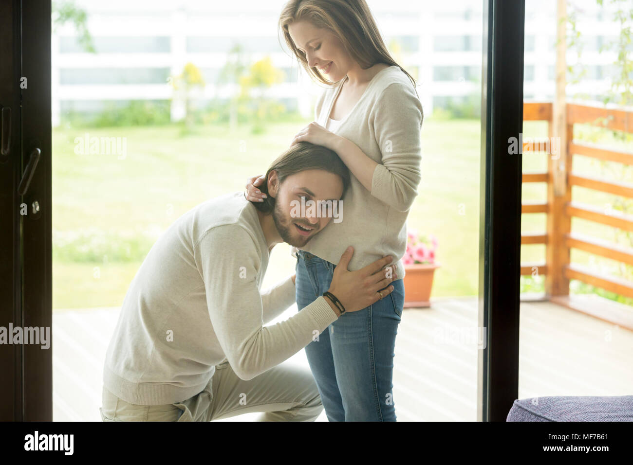 Happy dad-to-be puts ear to pregnant belly, pregnancy and men Stock Photo