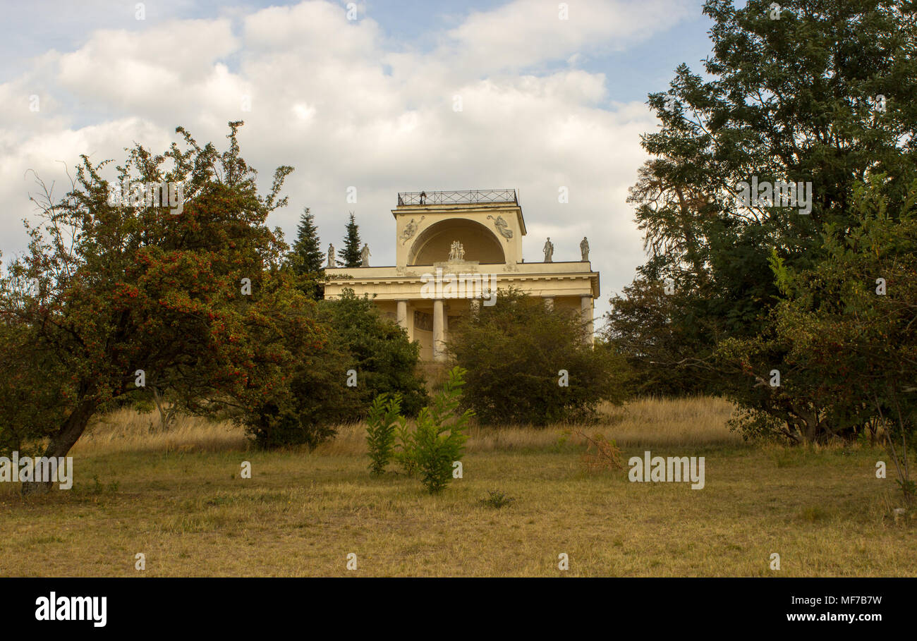 View on  the Apollo temple in the Czech republic. On the background is blue sky with white clouds. In the foreground are bushes and trees. Stock Photo