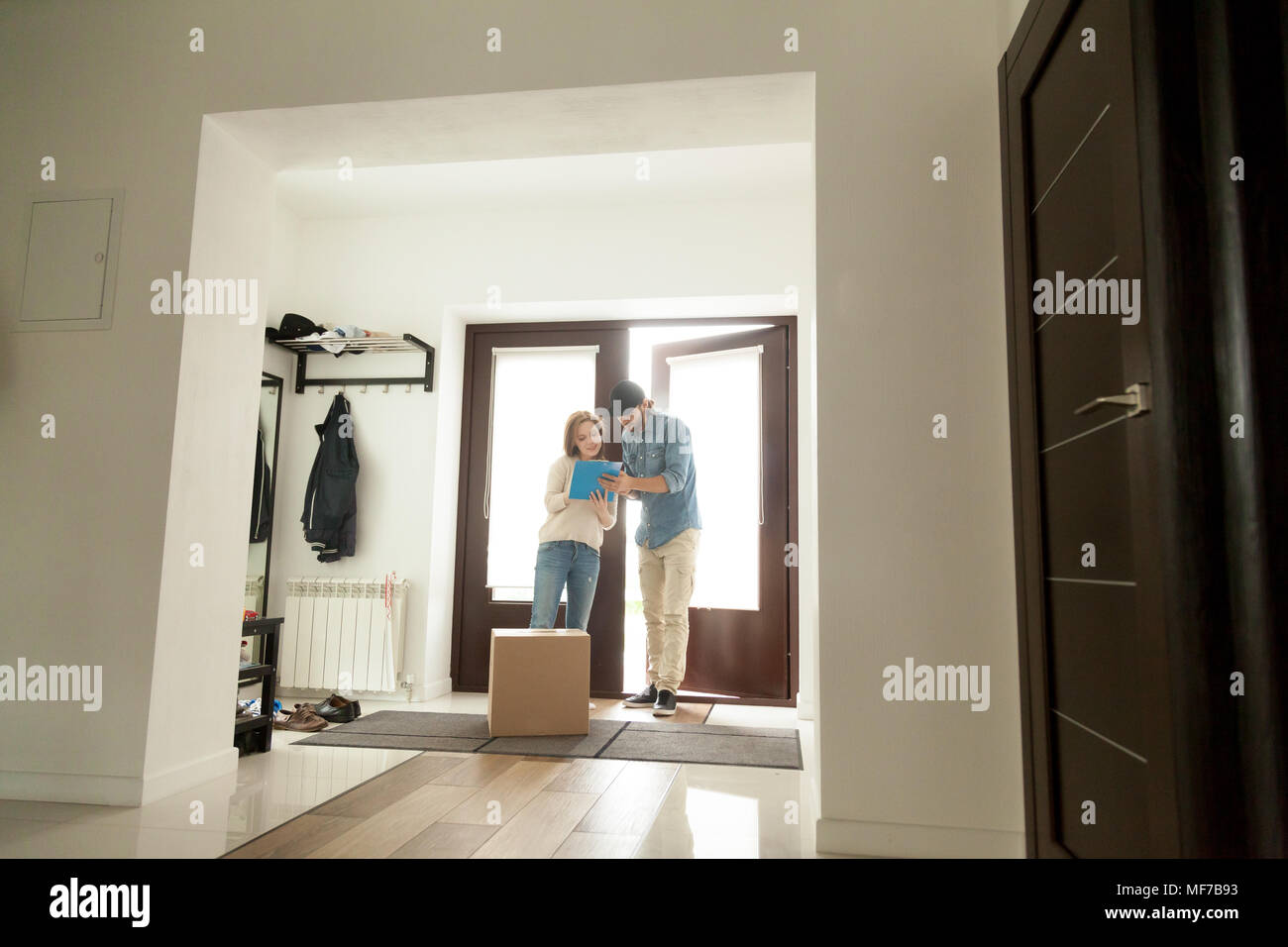 Woman signing for parcel receiving box from courier at home Stock Photo