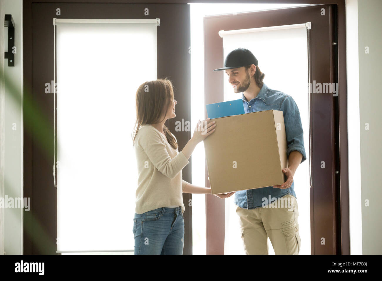 Smiling courier delivering parcel to young woman, delivery servi Stock Photo