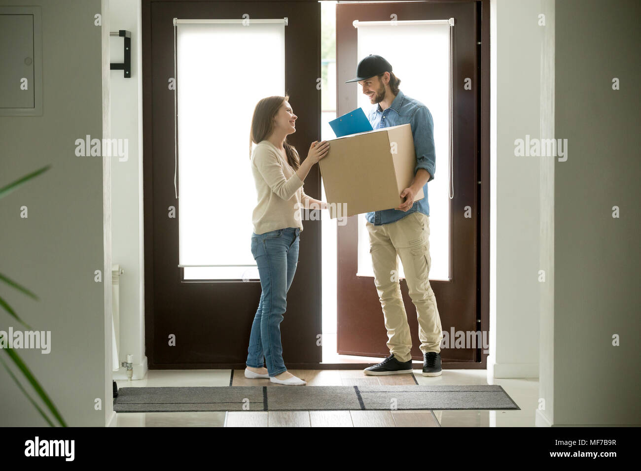 Happy woman receiving parcel from courier at home, delivery serv Stock Photo