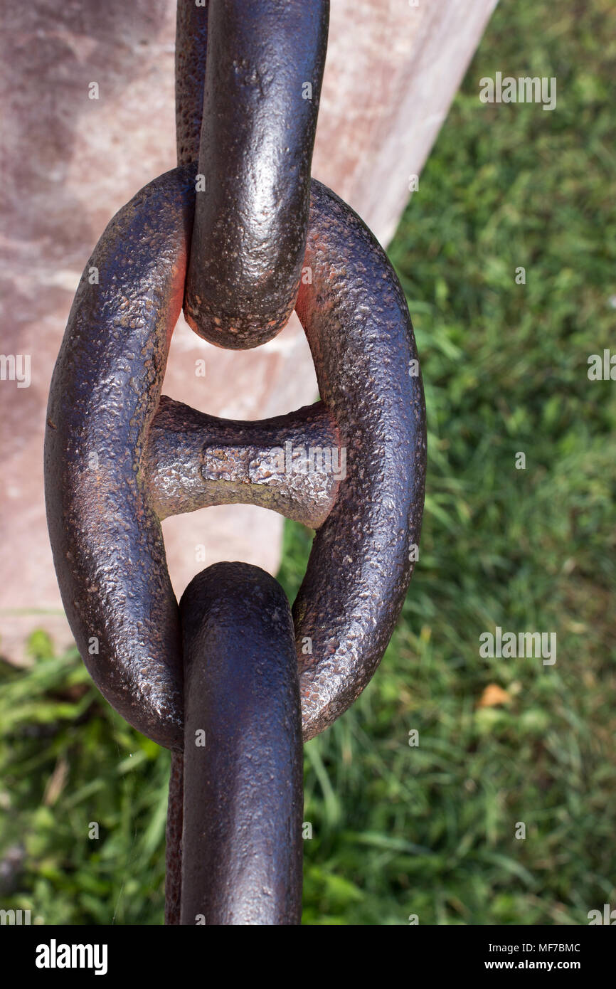 Detail of an old rusty chain with stone pillar on a green background. In the background is green grass. Stock Photo