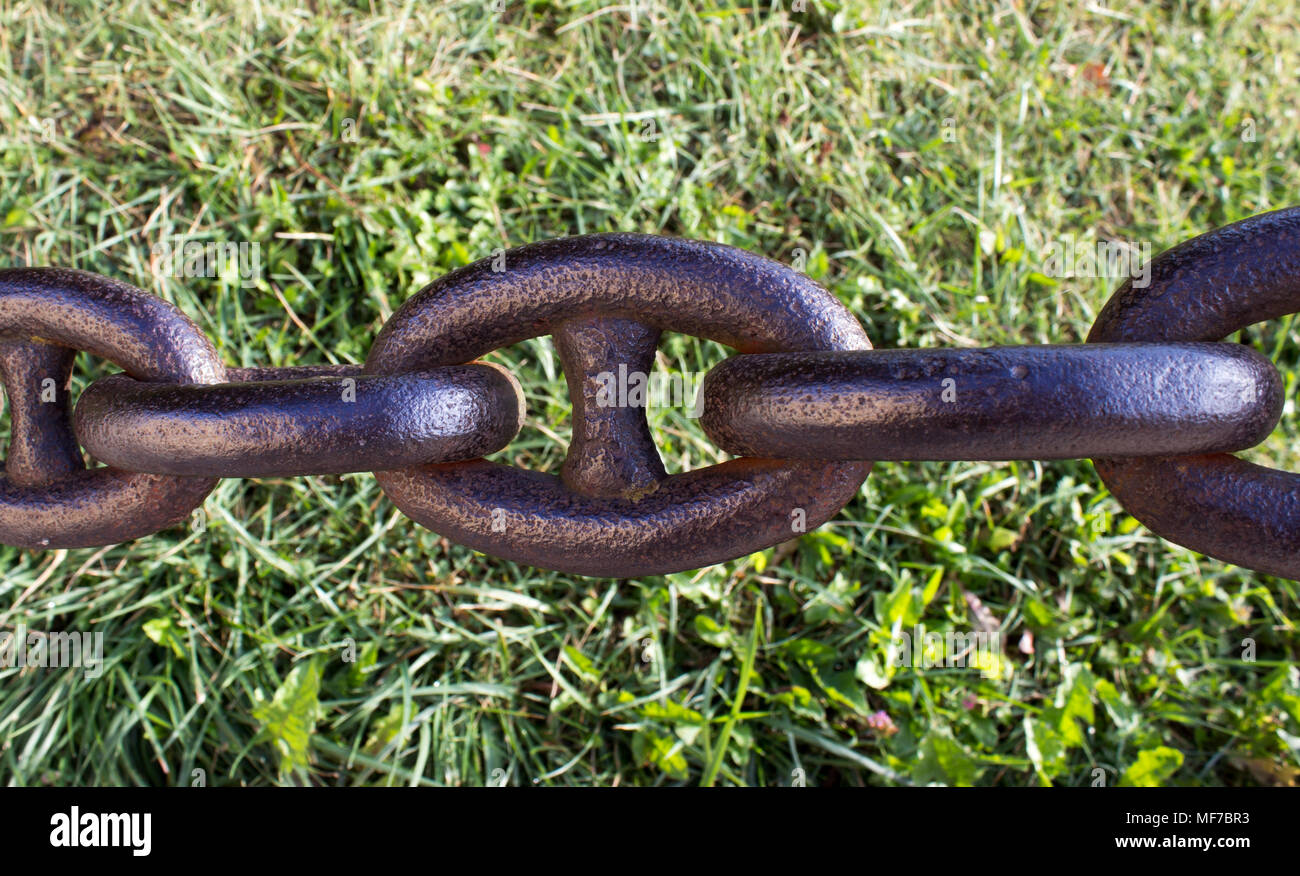 Detail of an old rusty chain on a green background. In the background is green grass. Stock Photo