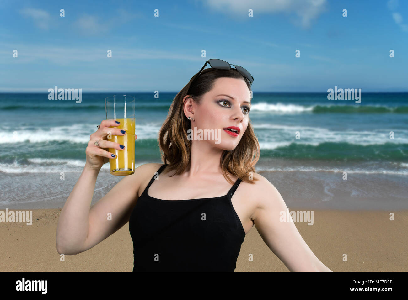 Drinking Orange Juice on the Beach. Attractive young women with a glass of orange juice posing on the beach. Stock Photo