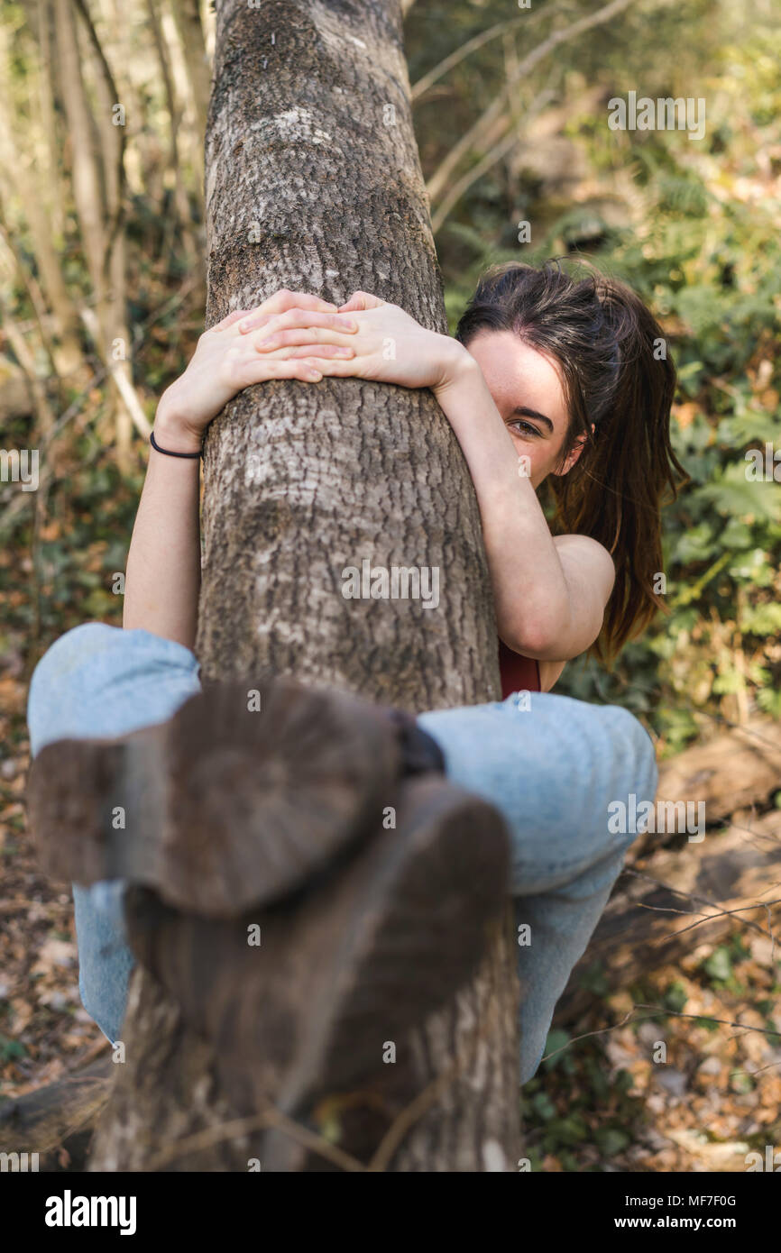 Happy young woman clutching a tree trunk Stock Photo