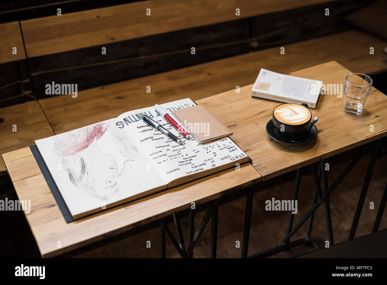 Table in a cafe with coffee mug, notebooks, pens and a glass of water Stock Photo