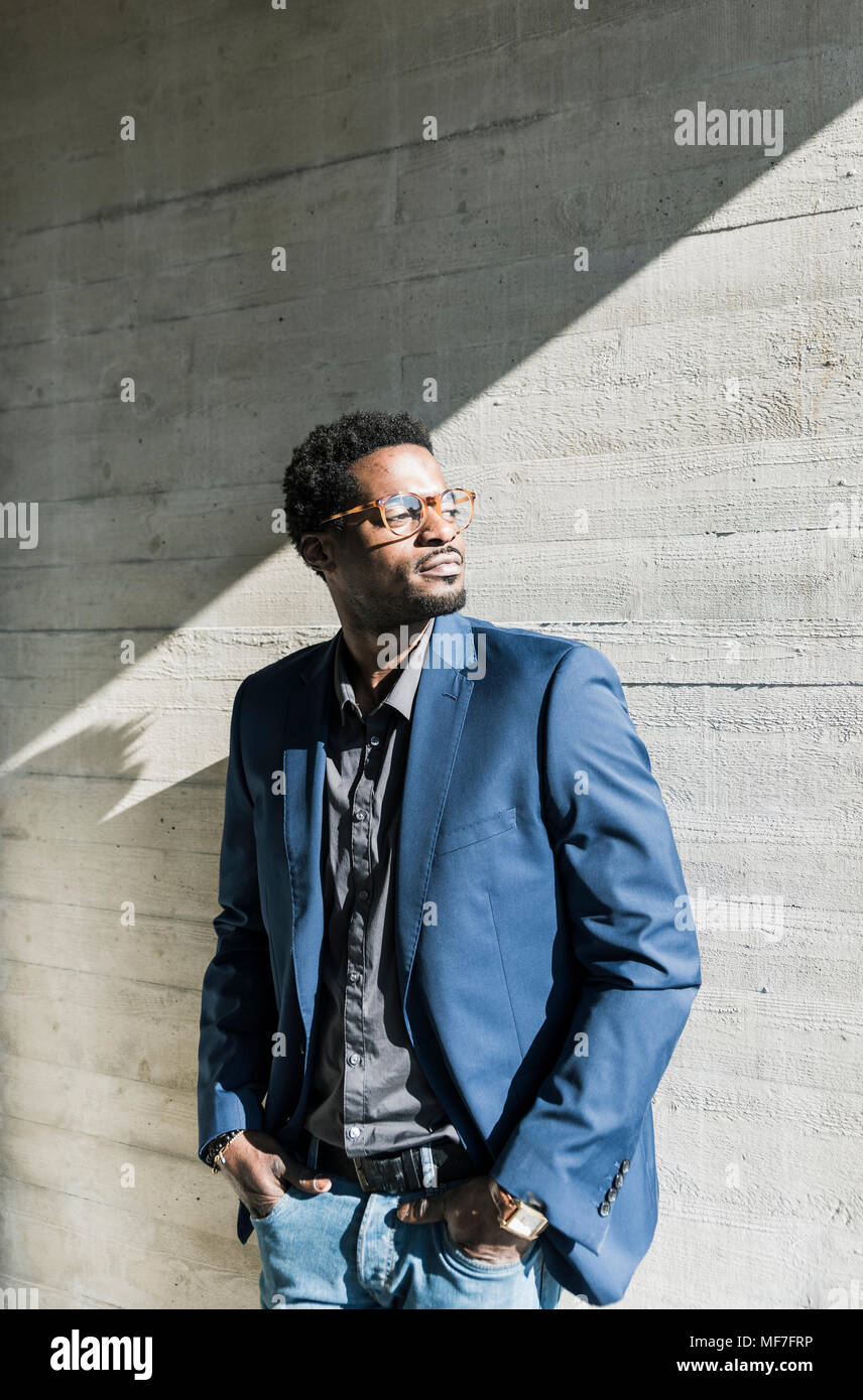 Businessman standing in sunshine at concrete wall looking away Stock Photo