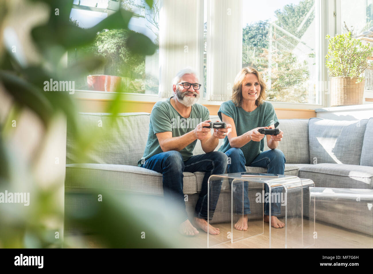 Happy mature couple sitting on couch at home playing video game Stock Photo