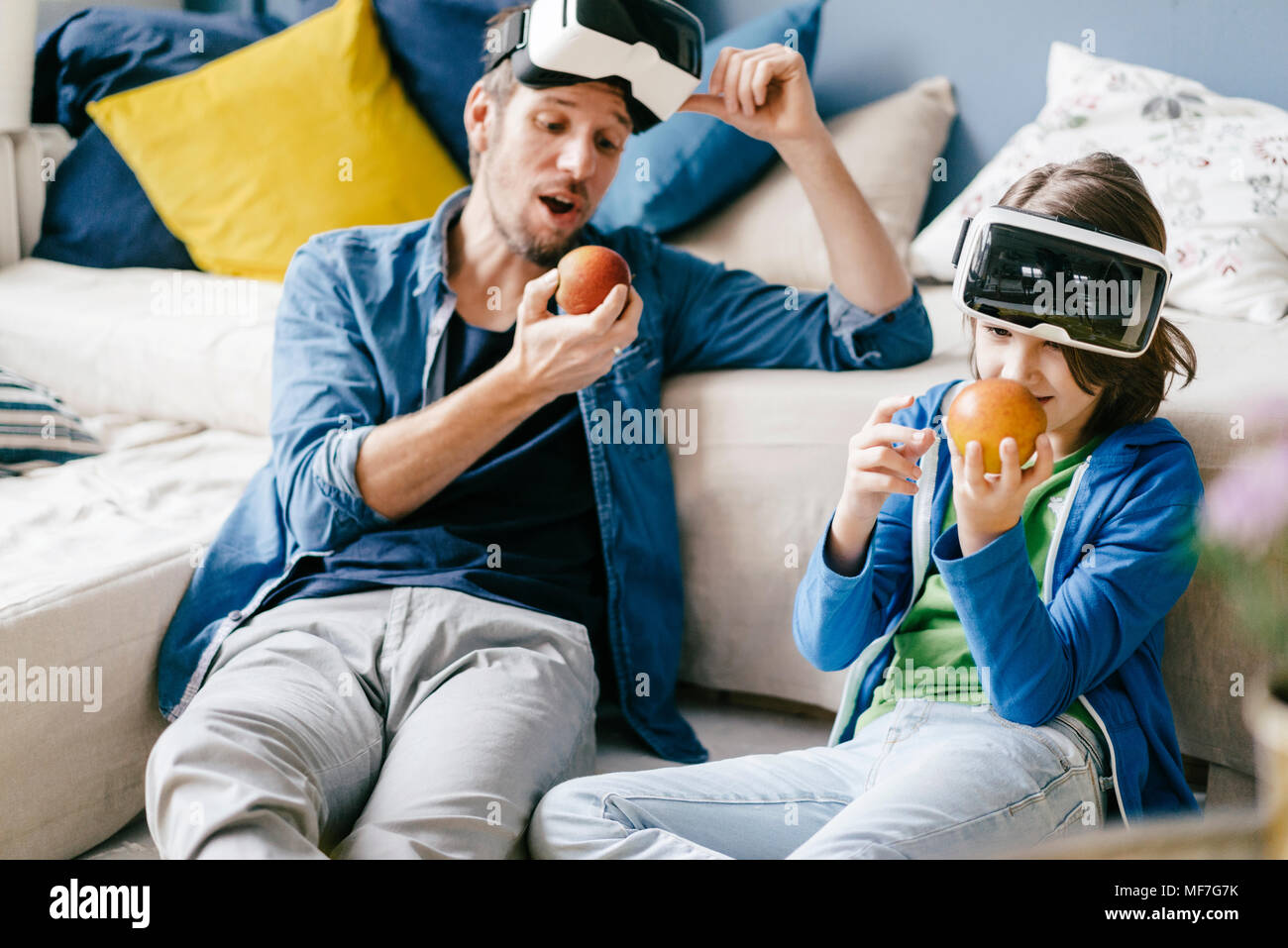 Father and son wearing VR glasses and eating apples at home Stock Photo