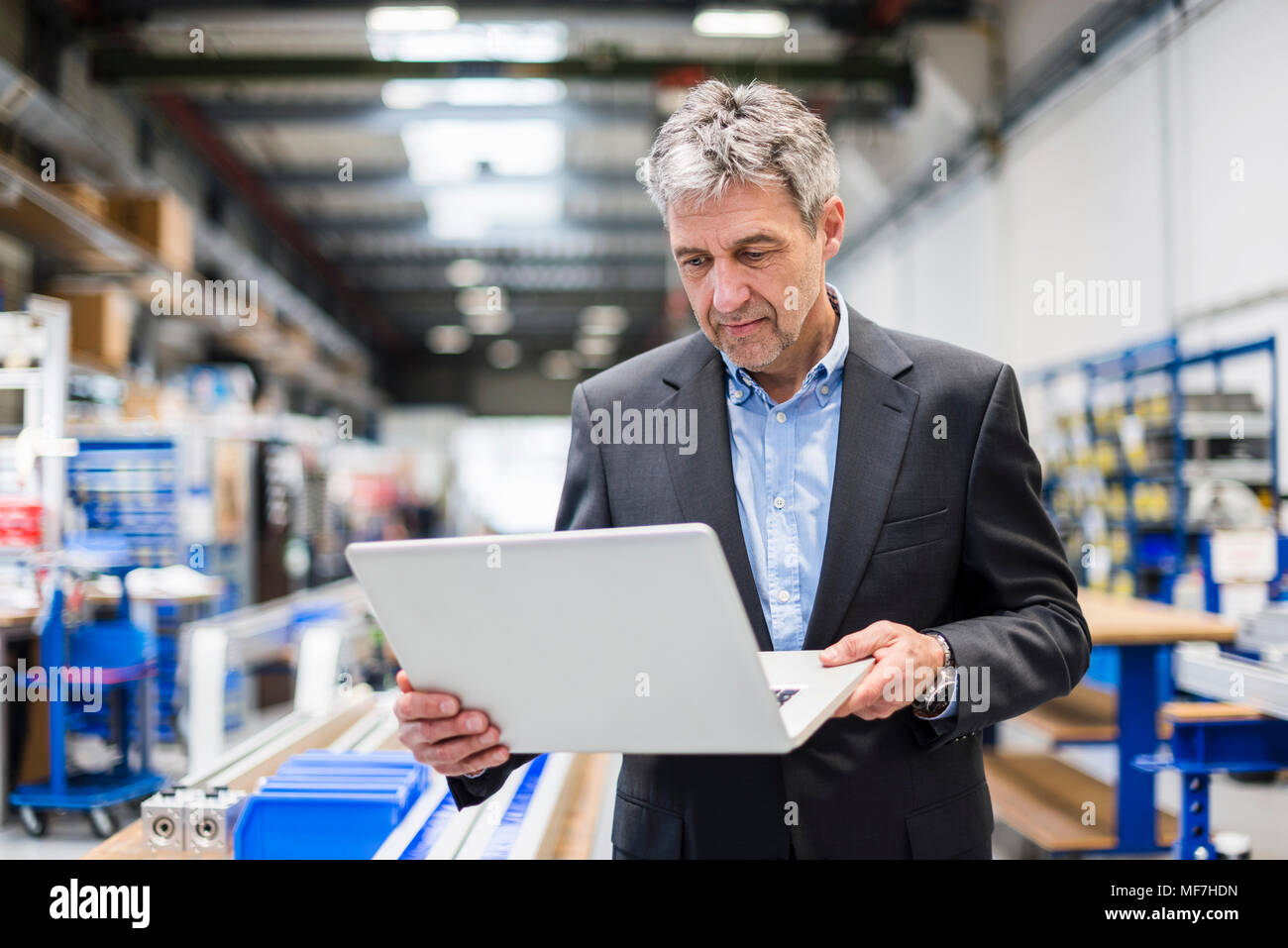 Businessman using laptop in production hall Stock Photo