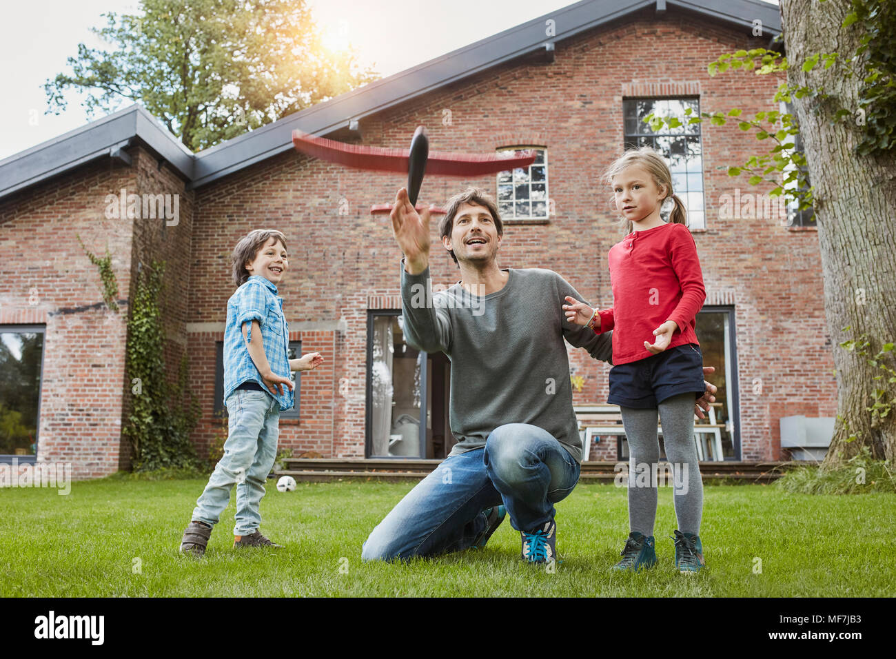 Father with two children playing with toy airplane in garden of their home Stock Photo