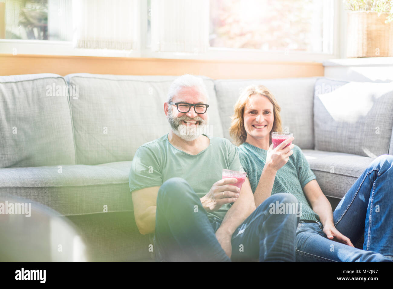Happy mature couple with healthy drinks in living room at home Stock Photo
