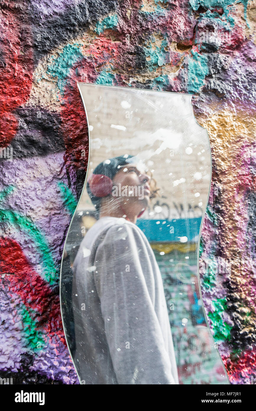 Mirror image of young man with headphones looking at graffiti Stock Photo