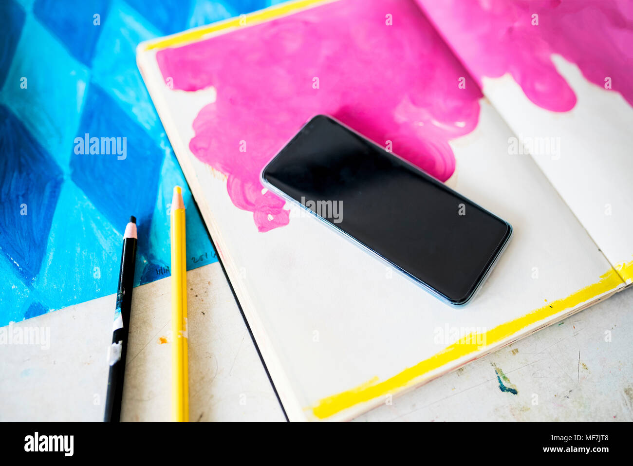 Smartphone lying on a notebook with a pink drawing in artist's studio Stock Photo