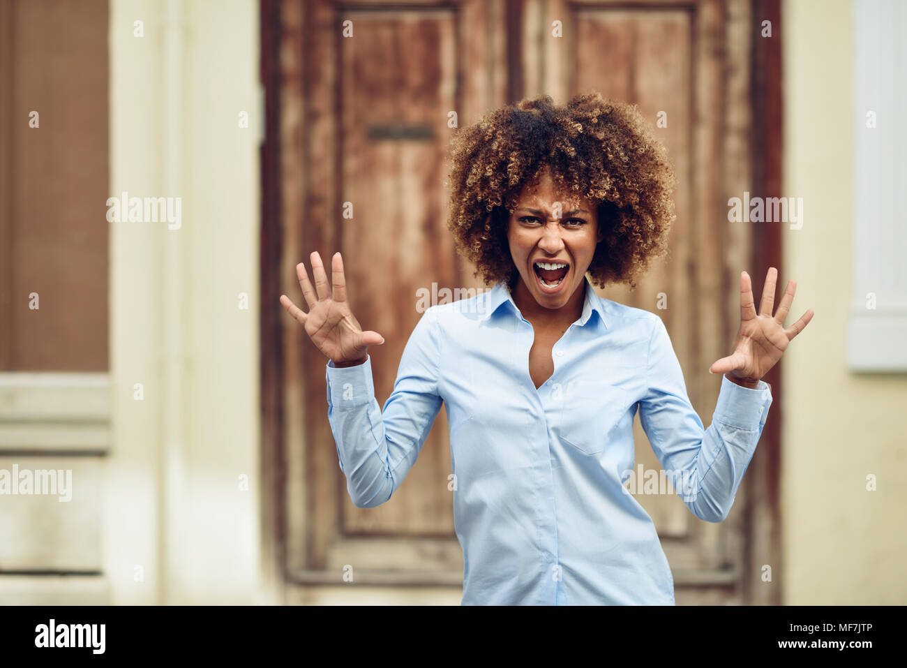 Spain, Andalusia, Malaga. Young black woman, afro hairstyle, screaming in the street. Girl wearing casual clothes in urban background. Expression conc Stock Photo