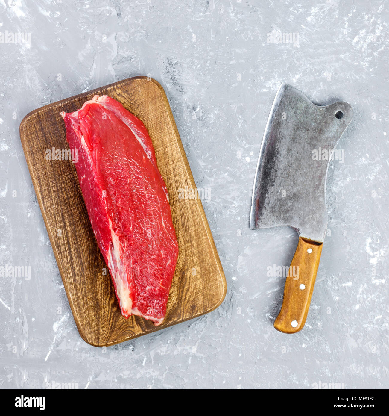 vintage cleaver and raw beef steak on gray concrete background Stock