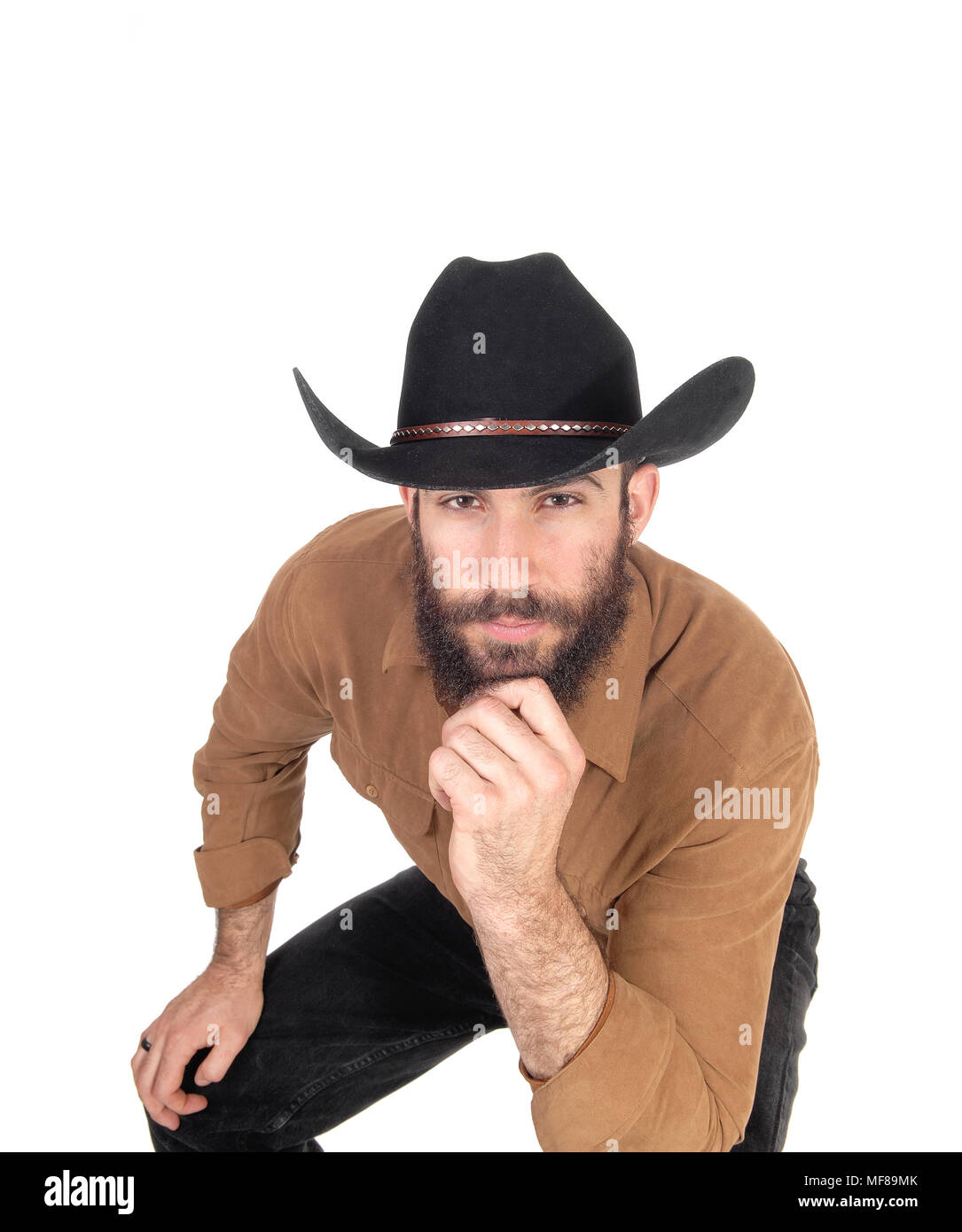 A young man sitting on a chair bending forwards wearing a black cowboy hat and one hand on his chin, isolated for white background Stock Photo