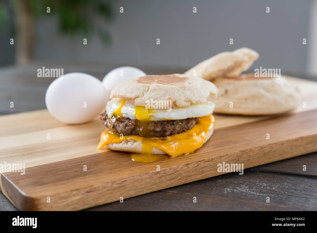 Sausage, egg and cheese breakfast sandwich with english muffin on cutting board with running yoke Stock Photo