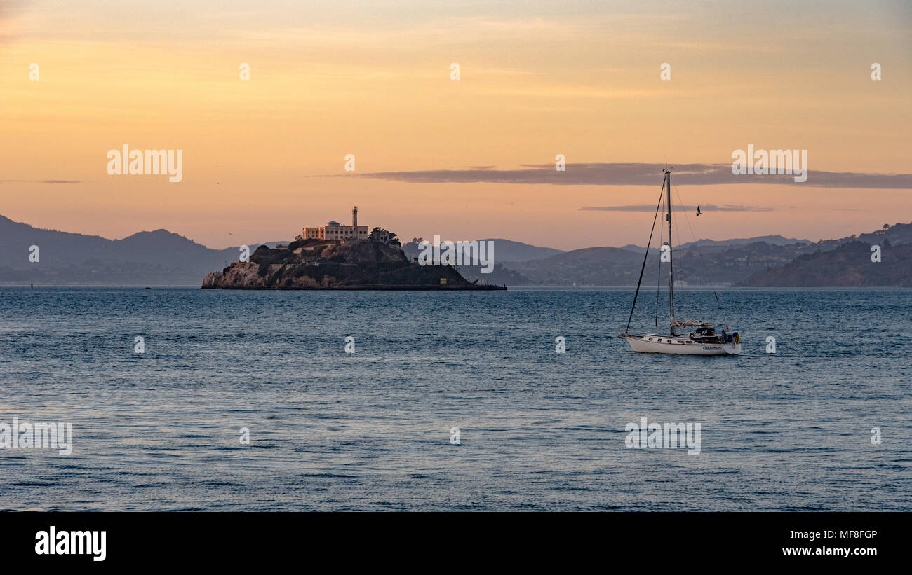 A sailboat goes by Alcatraz Island in San Francisco Bay at dusk Stock Photo