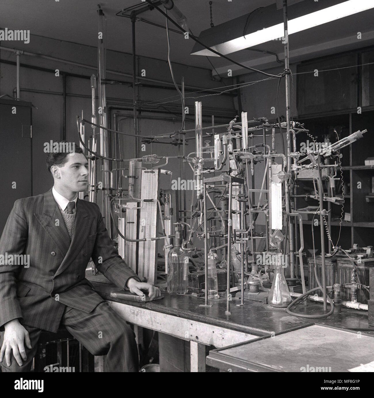 1948, historical, young male research scientist wearing a pin-stripe suit sitting next to the elaborate apparatus of pipes, tubes and glass bottles built for his research into the chemical properties of coal and carbon monoxide in a laboratory in the Dept of Coal, Gas, and Fuel Industries at Leeds University. Stock Photo