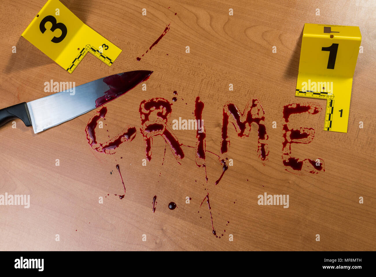 The word “crime” written in blood on a wood surface beside a bloody knife, both marked by crime scene evidence markers. Stock Photo