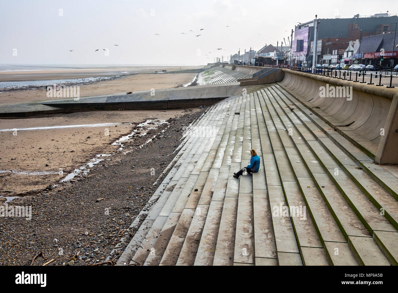 A Woman Sits Alone on the Steps of an Out Of Season Seaside Town (Concept Shot Posed by Model). Stock Photo