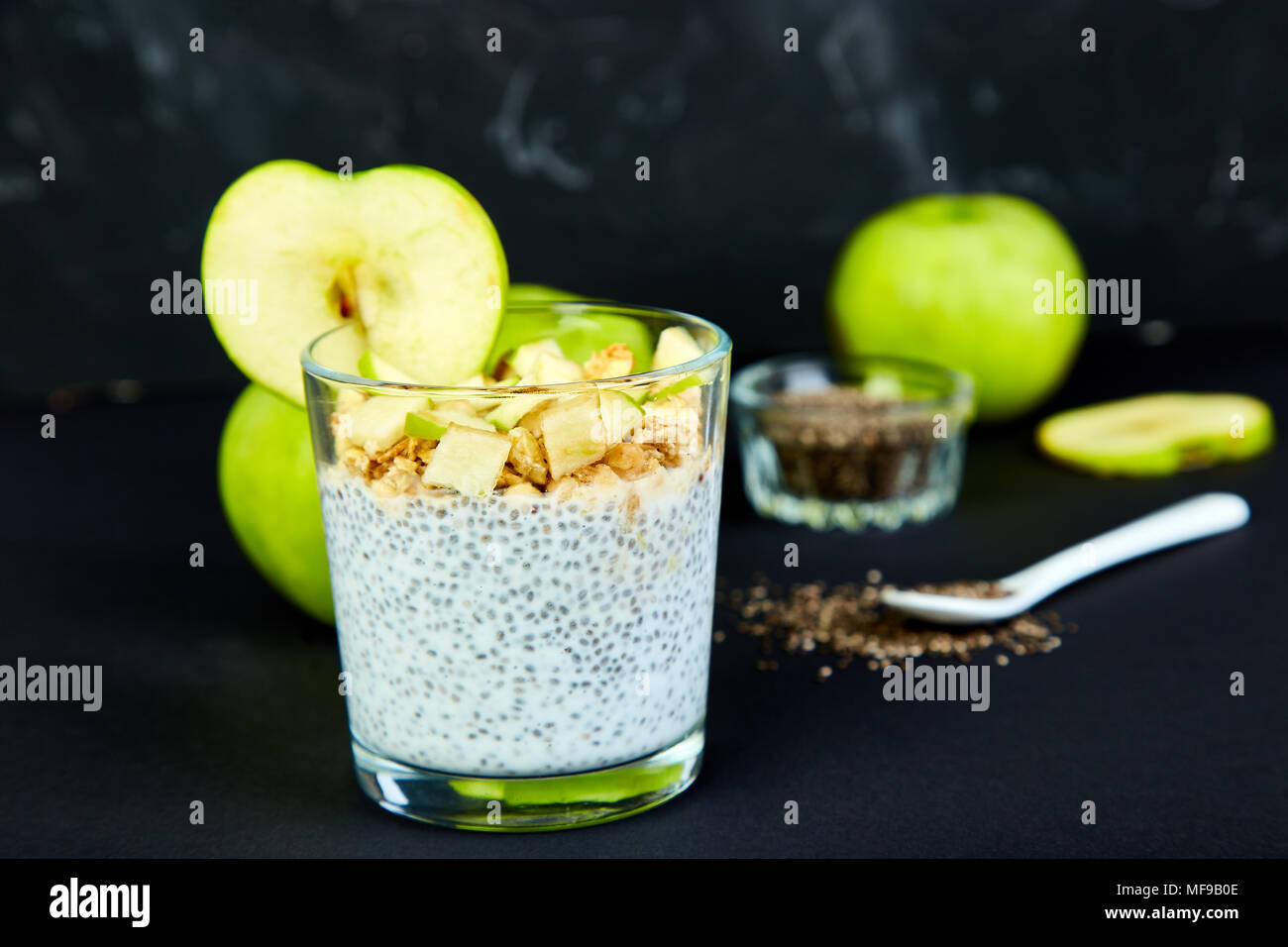 Healthy chia pudding with apples and granola in glass on black