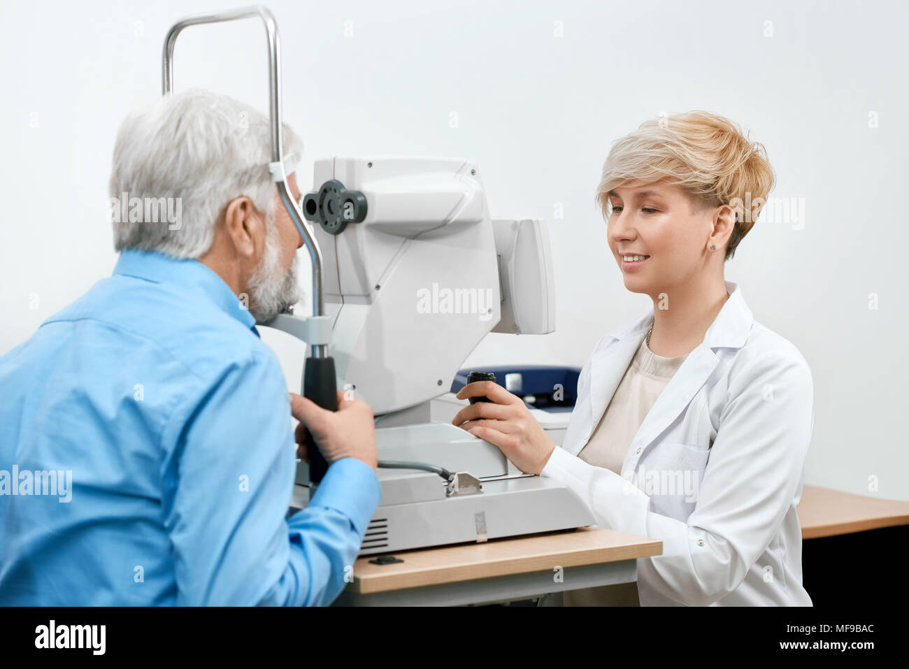Expirienced ophtalmological specialist treating old patient's vision. Doctor is working with medical equipment, looking skilled and professional. Oculist is working in white laboratory. Stock Photo