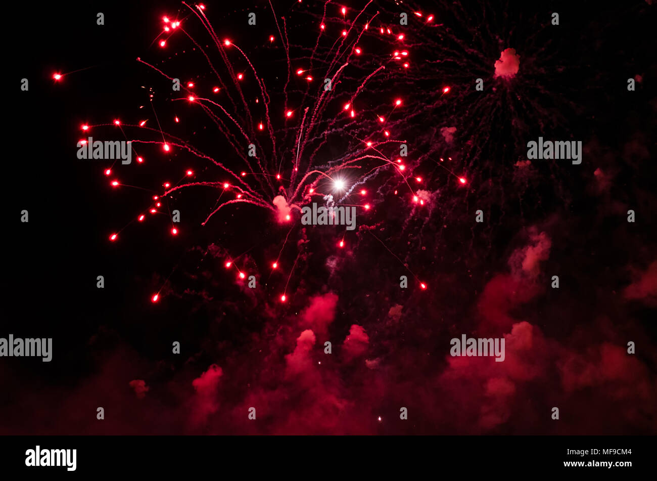 Fireworks with trails and smoke in red color against a black sky as background. Stock Photo