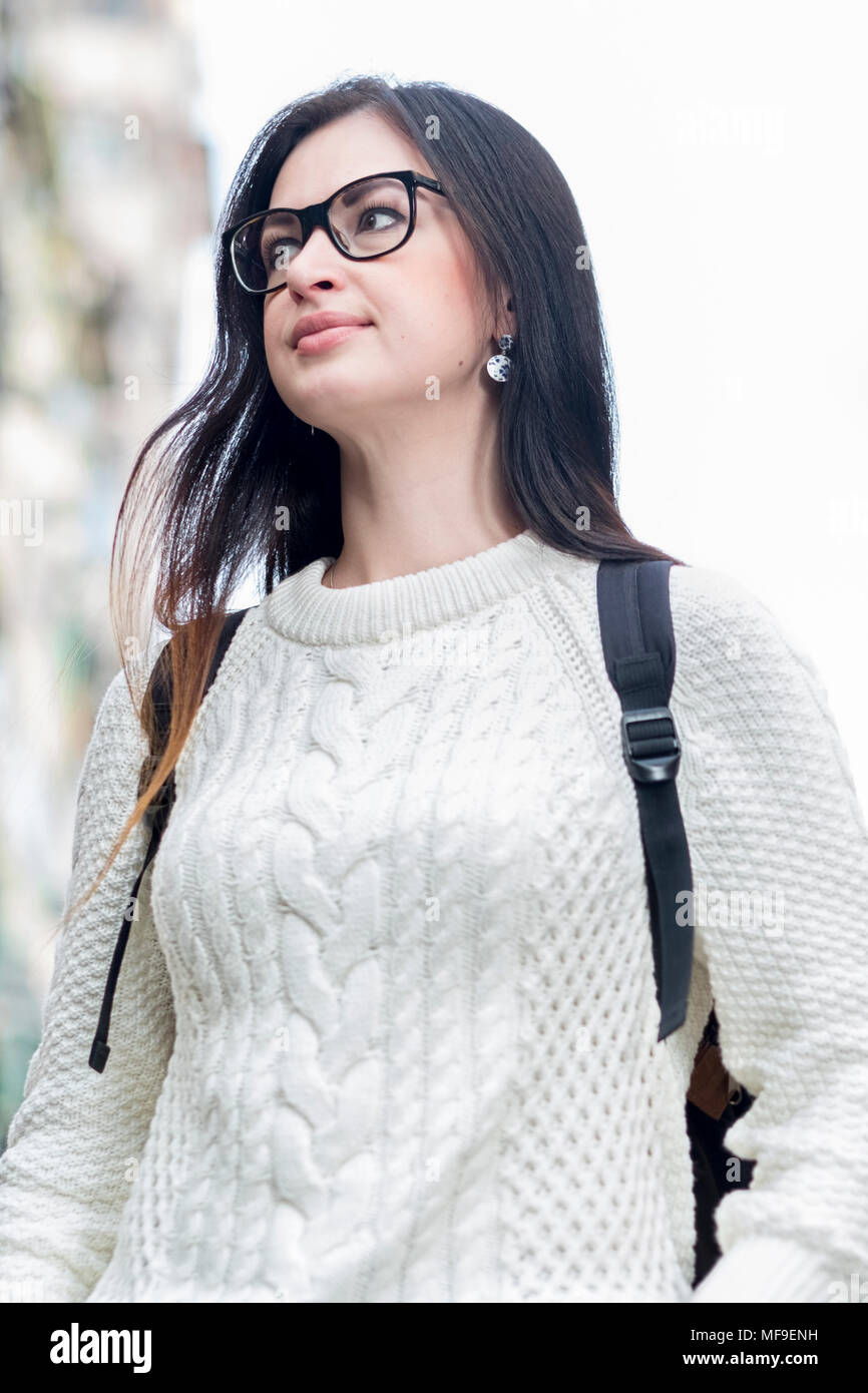 Attractive young single brunette girl tourist walking down street. Reflection of city lights in her glasses. Blurred buildings on background. Stock Photo