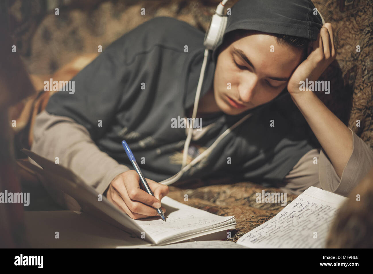 Teenage student guy studying lying on the sofa at home listening to music Stock Photo