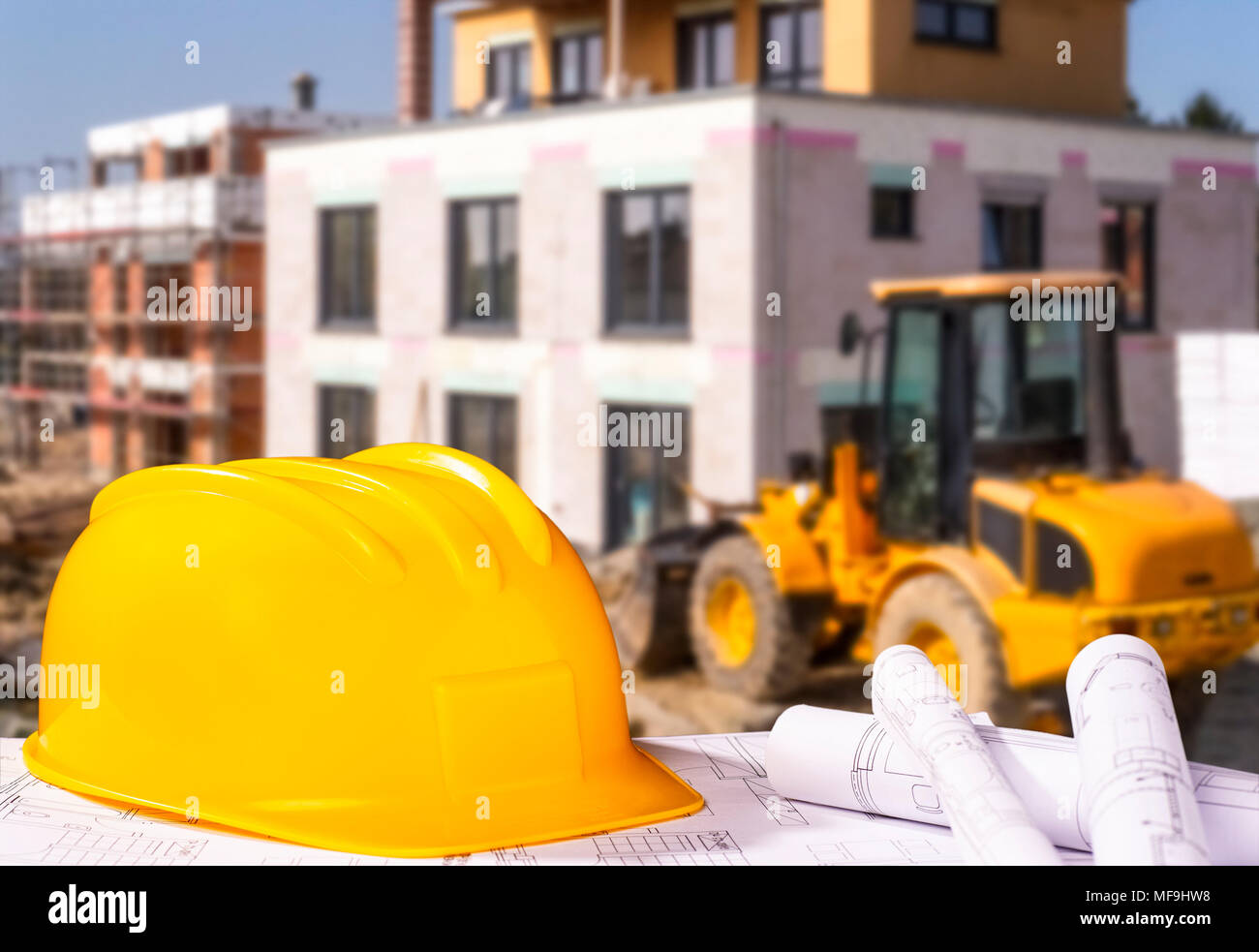 Helmet and blueprints and a construction site with wheel loader in the background Stock Photo