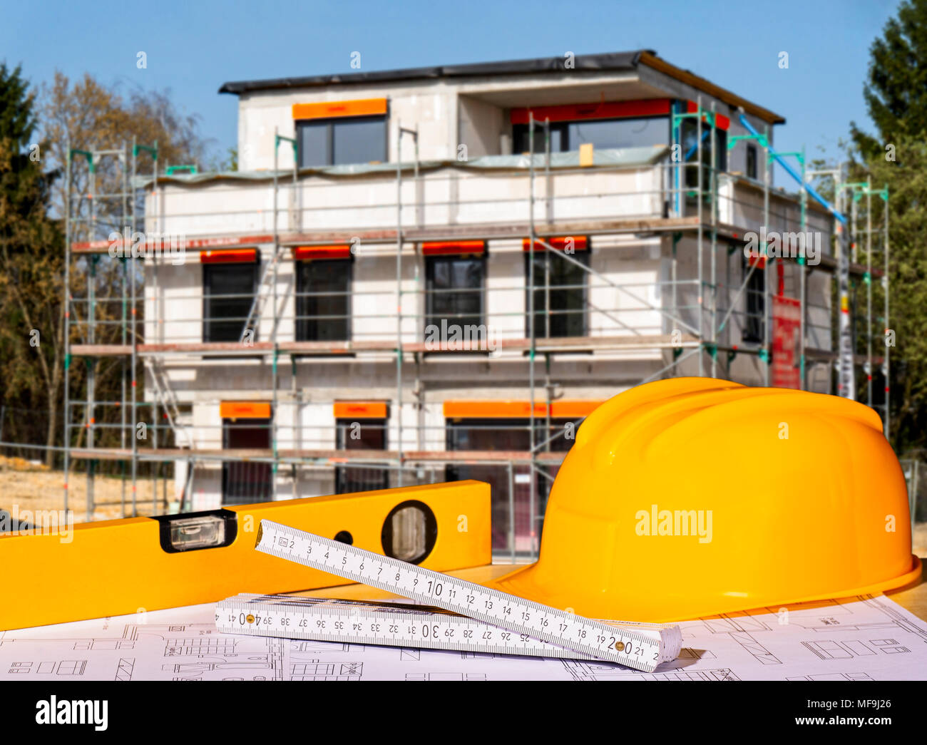 Helmet, spirit level, folding rule and building plans with a shell in the background Stock Photo