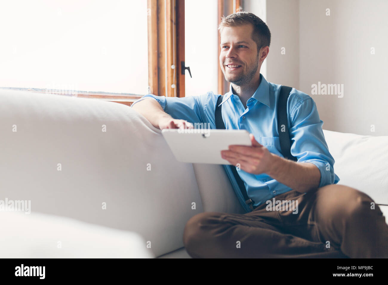 Handsome man sitting on sofa at home, using a digital tablet Stock Photo
